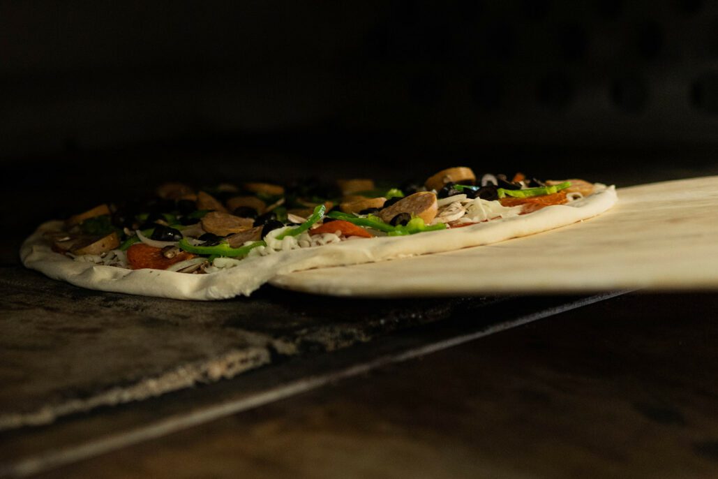 a pizza is slide into the oven on a pizza peel