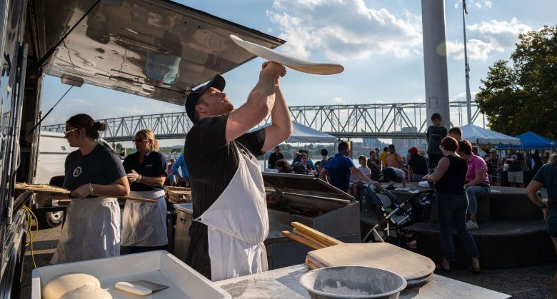 A Dewey's Pizza employees tossed pizza dough into the air in an open air kitchen