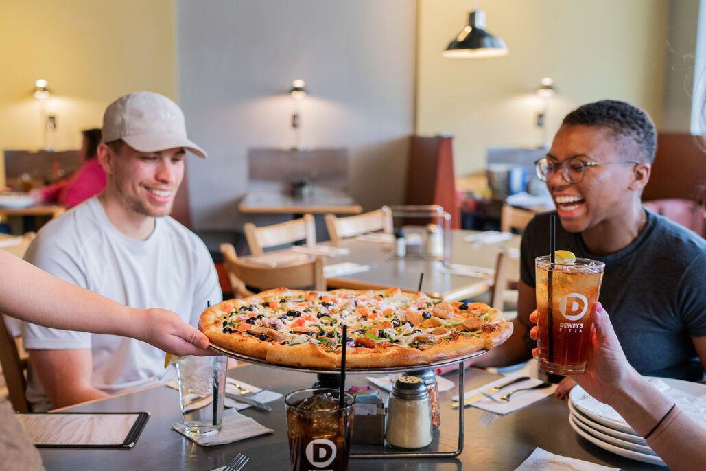 a family laughs as their pizza is delivered to the table