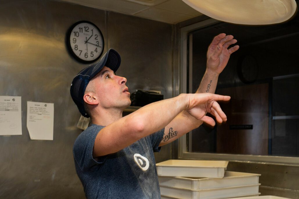 a dewey's employee tosses a pizza dough into the air