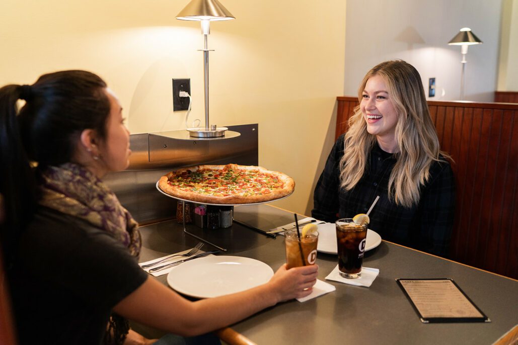 two women laugh over a pizza