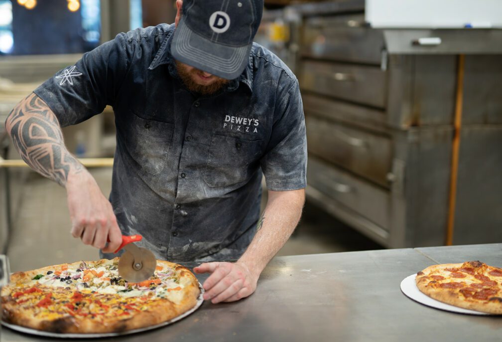 a dewey's employee cuts a pizza