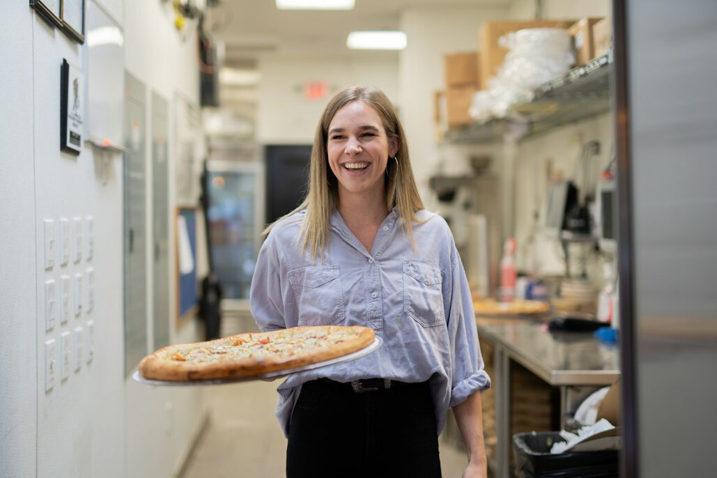 a woman smiles while holding a pizza